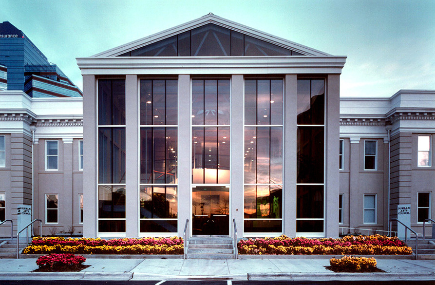 View of the front of the DAC building at dusk from across Morris Street, the sunset is reflected in the glass of the building. 