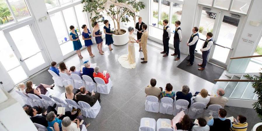 A wedding ceremony takes place in the pavilion with guests seated watching. The view is from above