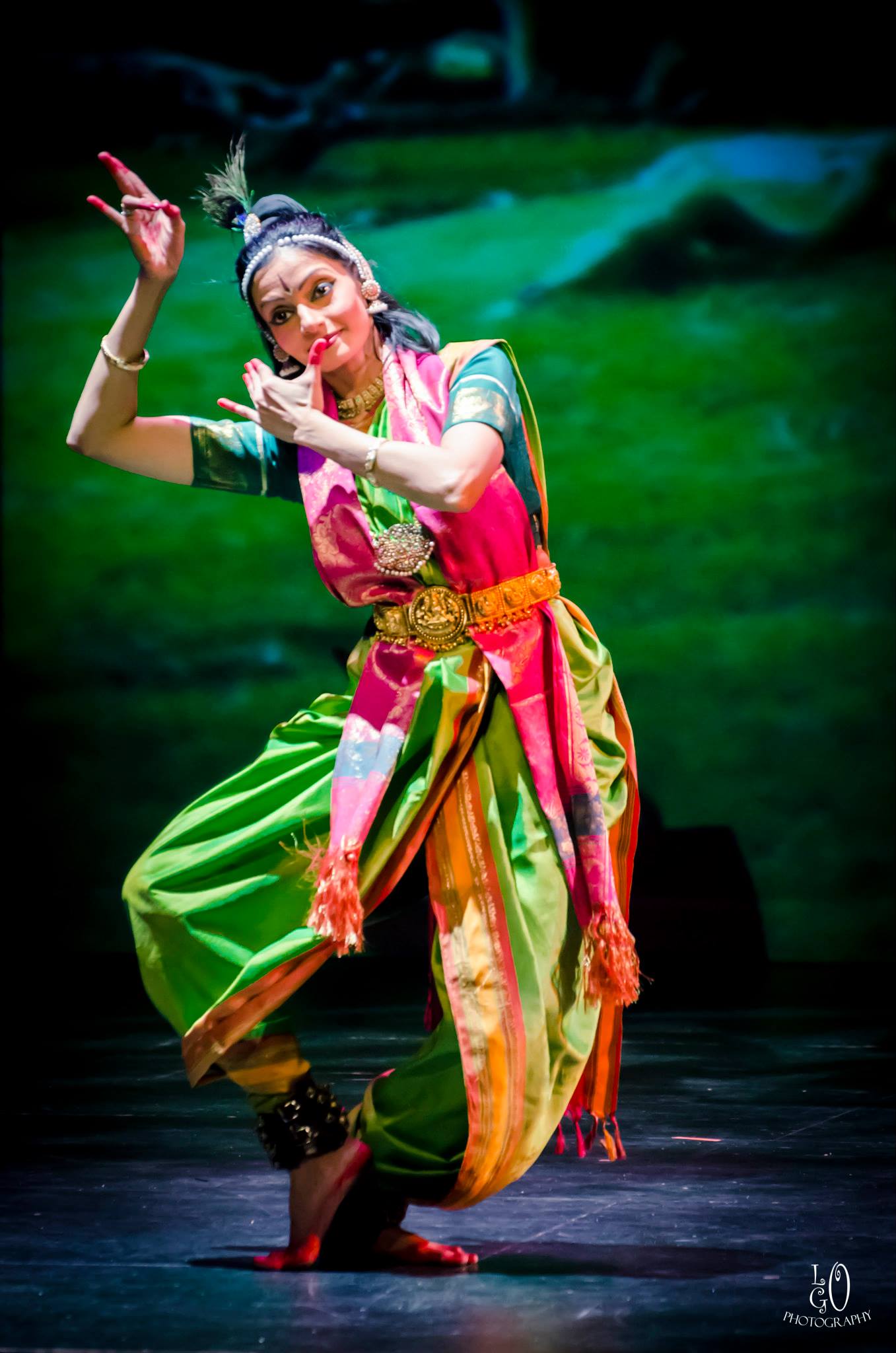 Indian dancer in colorful traditional clothing performs on stage with a green background