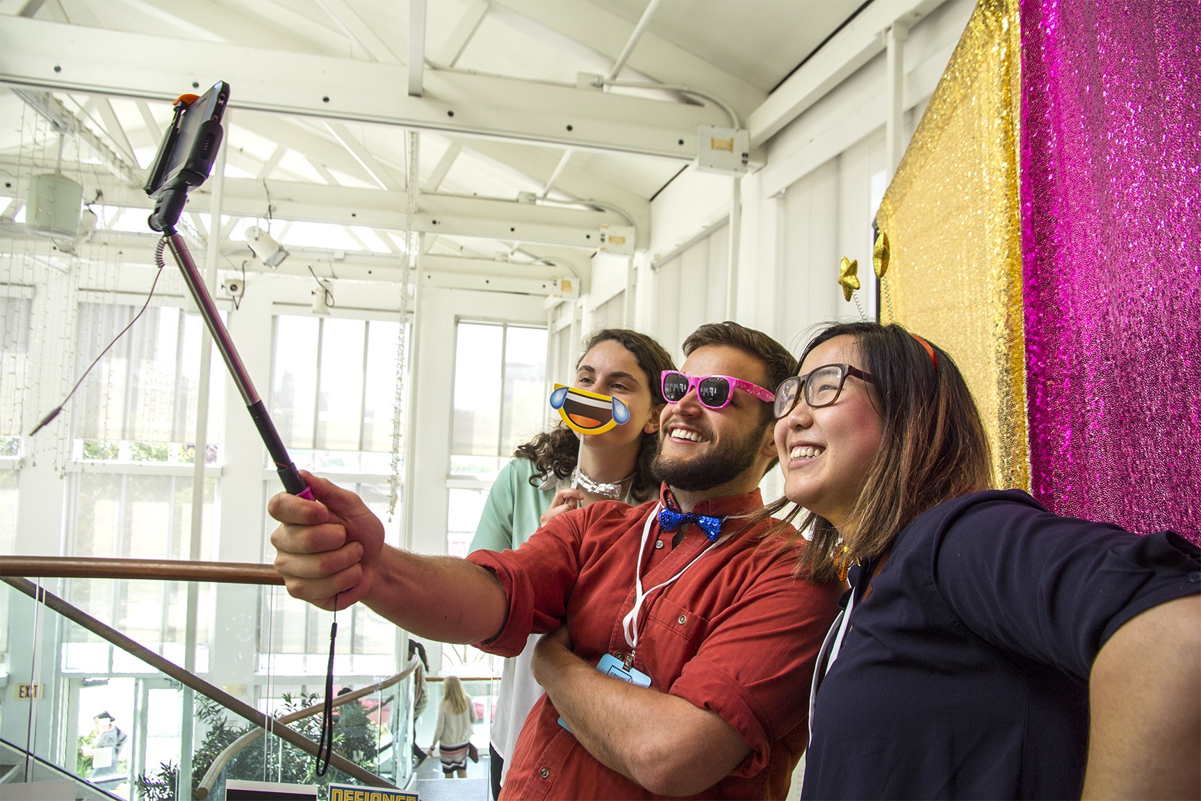 Picture of 3 people taking a selfie using fun props in front of a sparkly background