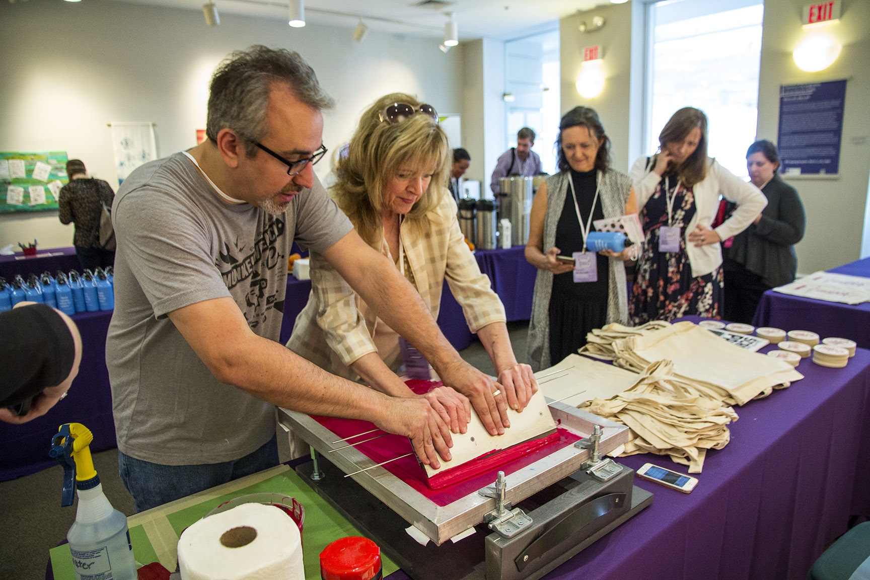 Man helps woman create a screen print on a tote bag during a break at a conference