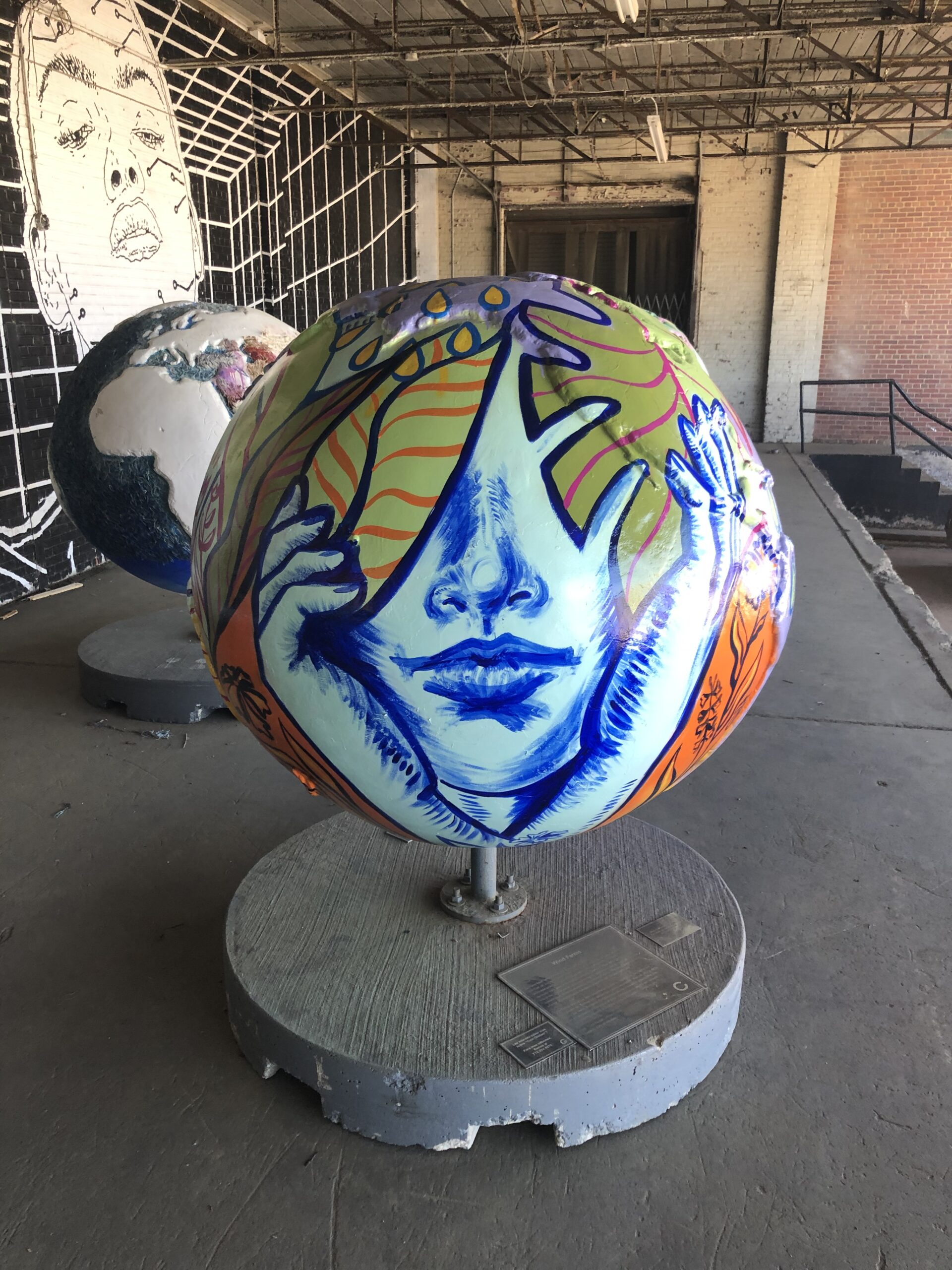 Globe painted to show a blue face cradled by blue hands with eyes hidden by tropical leaves